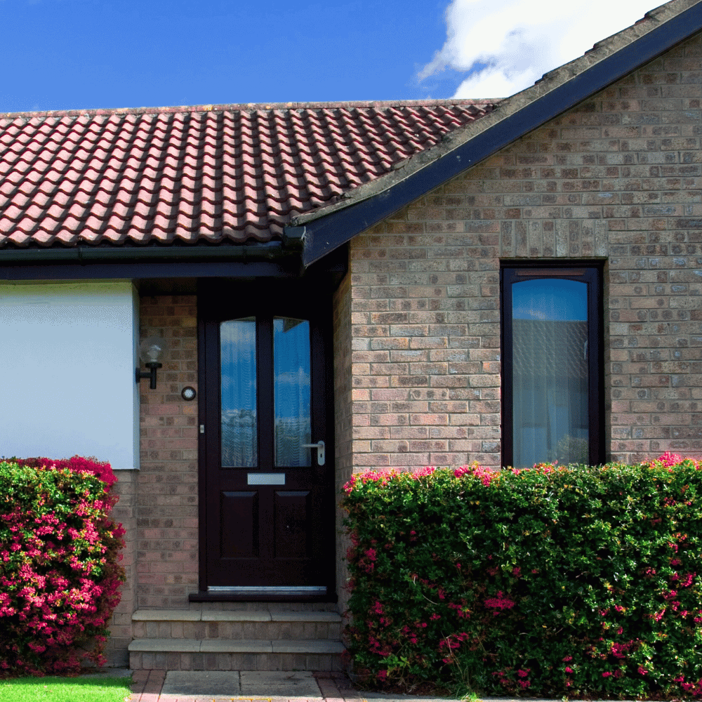 Brick façade, door and window, flowering shrubs.